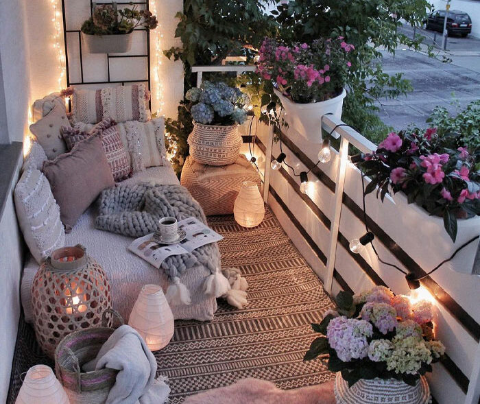 Bohemian balcony with furniture pillows sheets rug flowers and string lights
