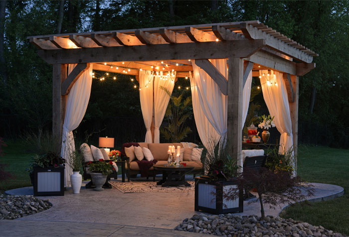 gazebo with curtain and string lights and furniture with white pillows and flowers
