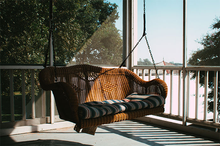 A brown porch swing with a striped pillow placed on it