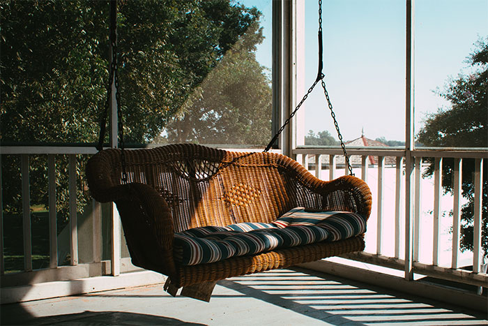 A brown porch swing with a striped pillow placed on it A brown porch swing with a striped pillow placed on it