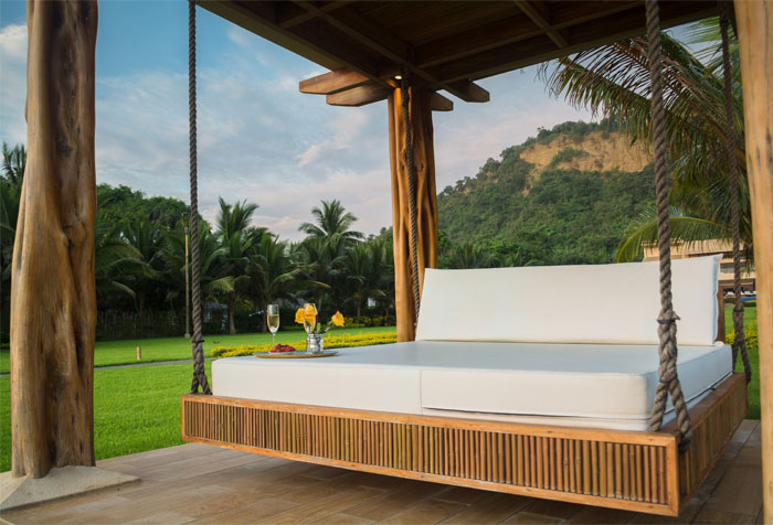 A rope-based brown wooden hanging porch swing with white bed A rope-based brown wooden hanging porch swing with white bed