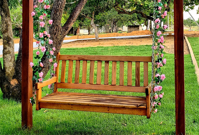 A chain-based brown wooden pergola porch swing with rose decorations in a garden A chain-based brown wooden pergola porch swing with rose decorations in a garden
