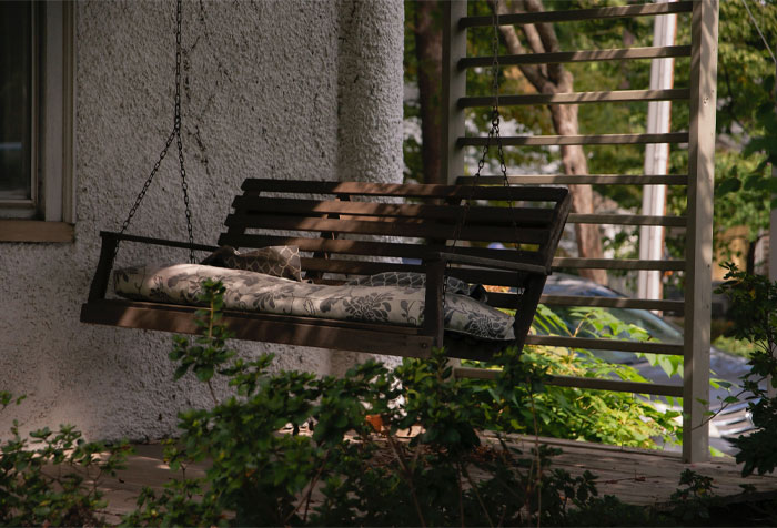 A chain-based rustic wooden porch swing with a gray flower pillow placed on it