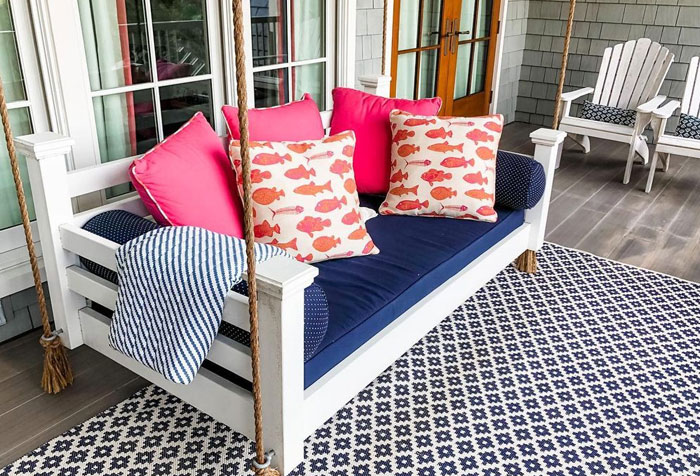 A rope-based white porch swing with a blue crib mattress and red fish symbol pillows