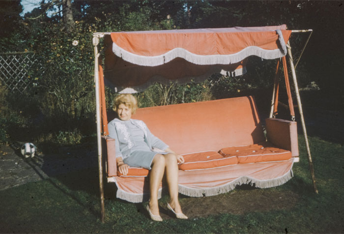 A lady wearing a blue dress sitting on a bright peach standing porch swing