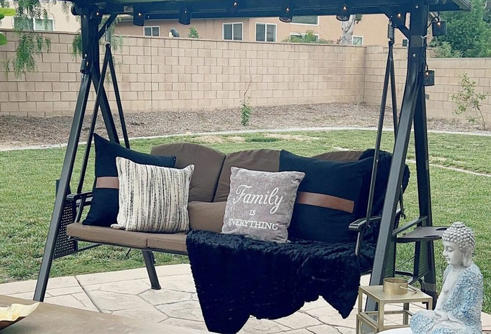 Metal-based black canopy porch swing with a brown mattress along with black and brown pillows Metal-based black canopy porch swing with a brown mattress along with black and brown pillows