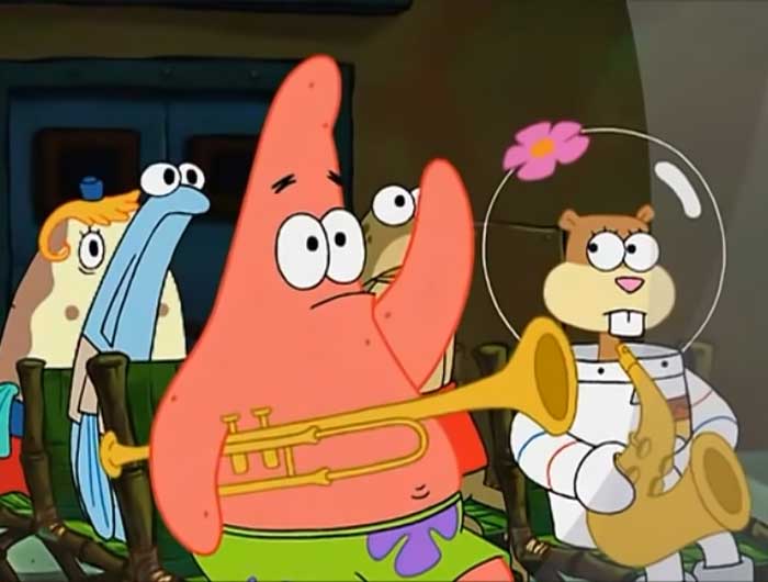 Patrick raising his hand while holding a trumpet under his other hand