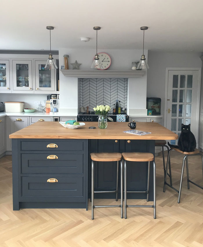 gray kitchen island with wooden countertop, bar chairs beside and extra storage space