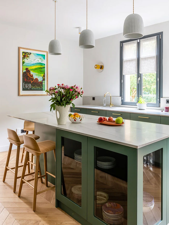 green wooden kitchen island with wooden bar chairs beside and fruits with flowers placed on it