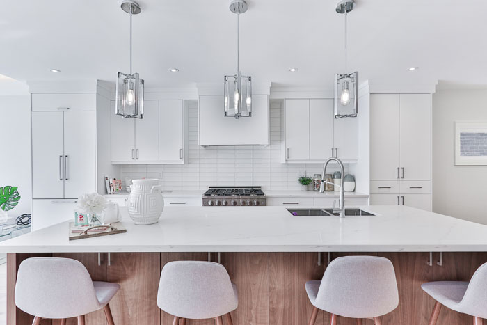 bright kitchen with wooden kitchen island with white countertop and white bar chairs beside