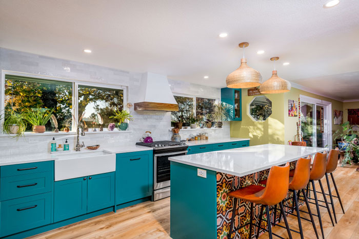 kitchen with blue cabinets and blue and ornamental galley kitchen island with orange bar chairs beside