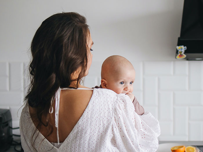 Woman holding her baby in a kitchen, illustrating family demands about giving her baby to her sister. Woman holding her baby in a kitchen, illustrating family demands about giving her baby to her sister.