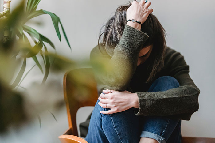 Woman sitting alone in a chair looking distressed, representing family demands about giving baby to sister. Woman sitting alone in a chair looking distressed, representing family demands about giving baby to sister.