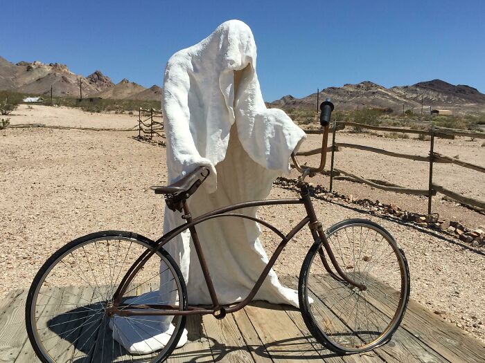 An Outdoor Sculpture Of A Specter And A Bicycle In The Desert