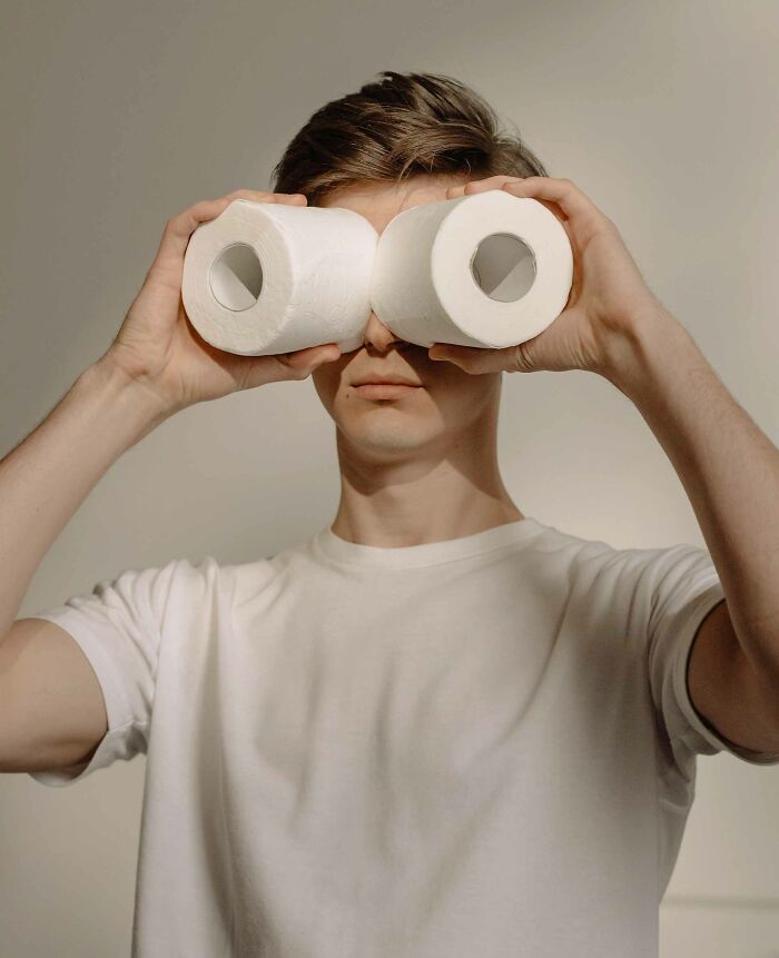 A man in a white t-shirt holds two white tissue rolls
