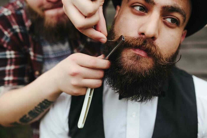 A barber shaves a bearded man in a vintage atmosphere