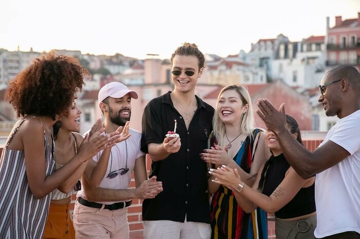 A joyful young man with a birthday cupcake in hand during a party with happy, diverse friends