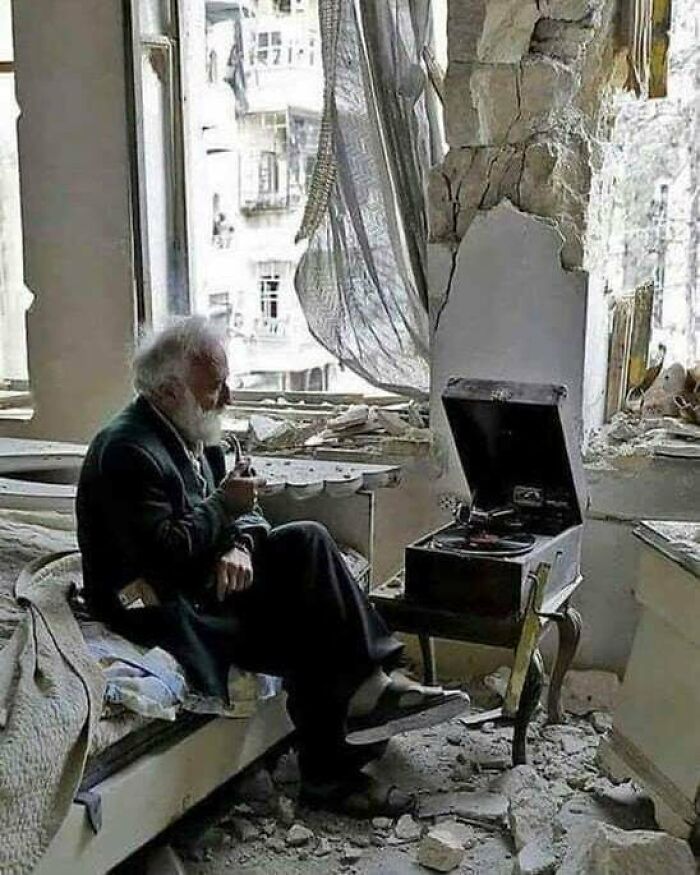 Hombre escuchando su fonógrafo en su dormitorio destruido en Alepo, Siria. 2017 por Joseph Eid