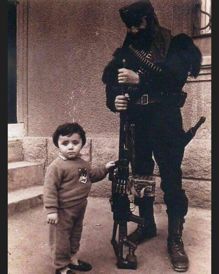Pavlik Manukyan, Armenian War Hero During The First Nagorno-Karabakh War In The Early 1990's, Seen During A Visit To His Family Away From The Frontline. He Is Posing Armed With A Pkm Machine Gun, Standing Next To His Son