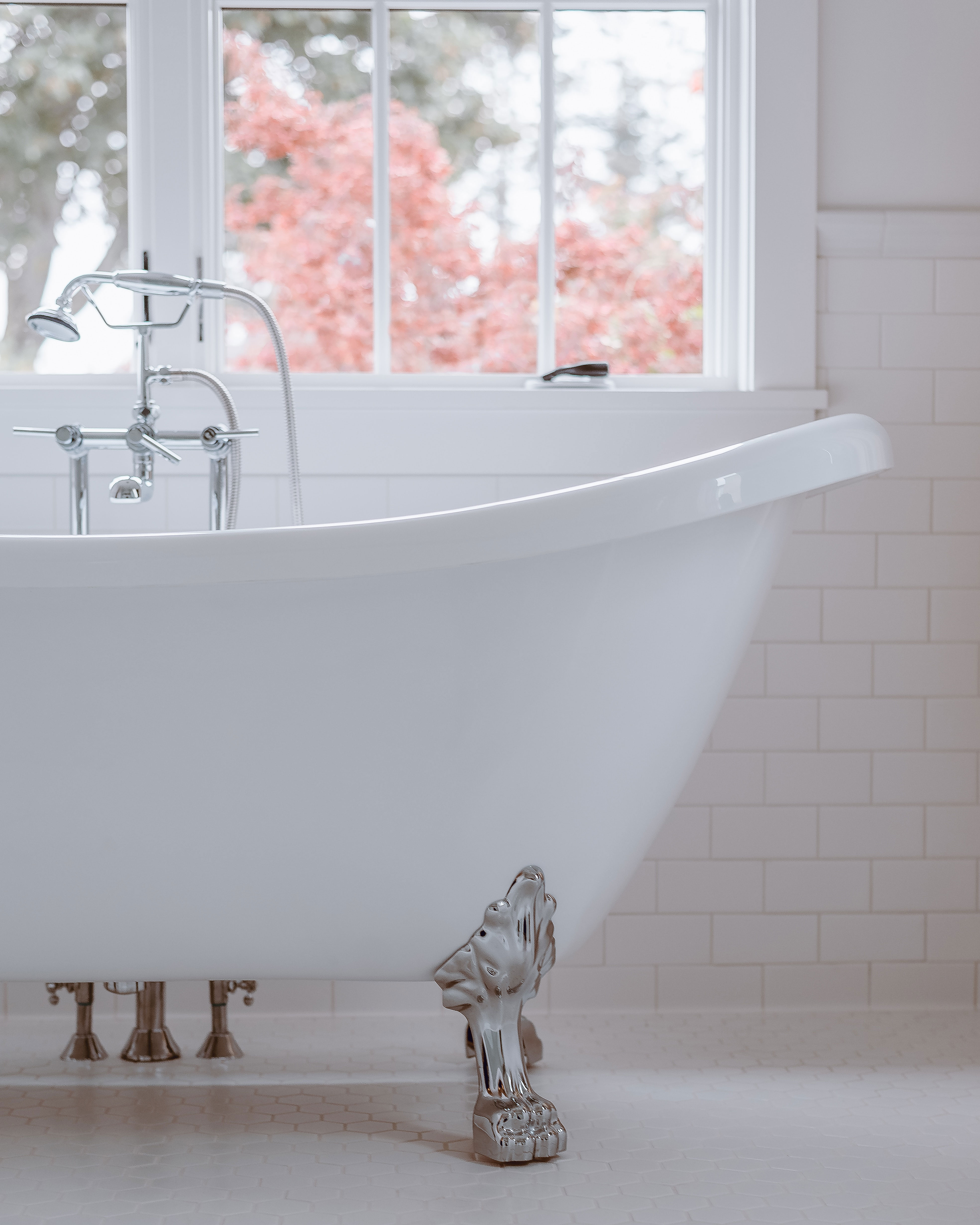 A white clawfoot tub on a white tile floor and white tile walls.