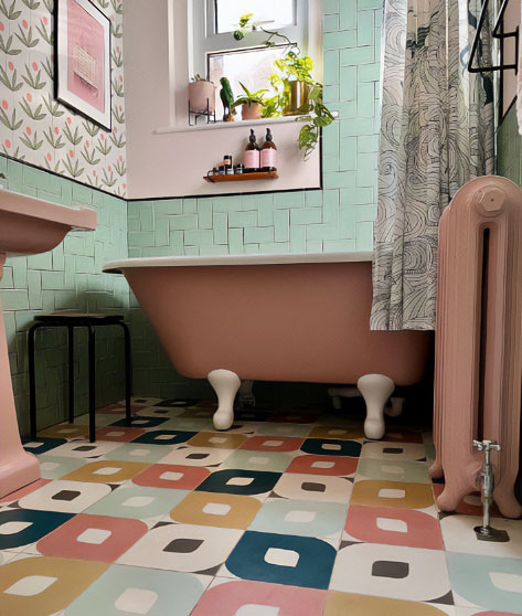 Pastel pink clawfoot tub standing on ornamental floor.