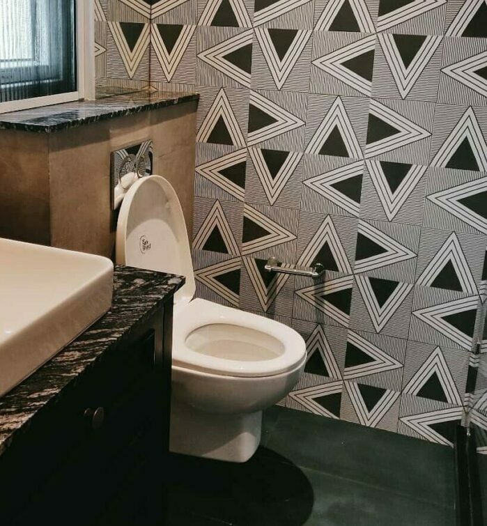 Bathroom with black geometric wallpaper, white toilet, and sink featuring a dark marble countertop in a modern space. Bathroom with black geometric wallpaper, white toilet, and sink featuring a dark marble countertop in a modern space.