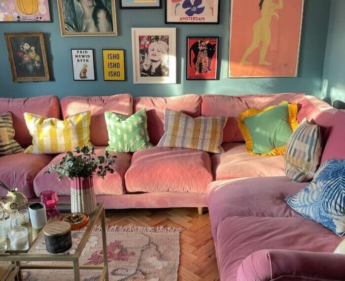a maximalist living room with a pink sofa, pillows, and paintings on the wall