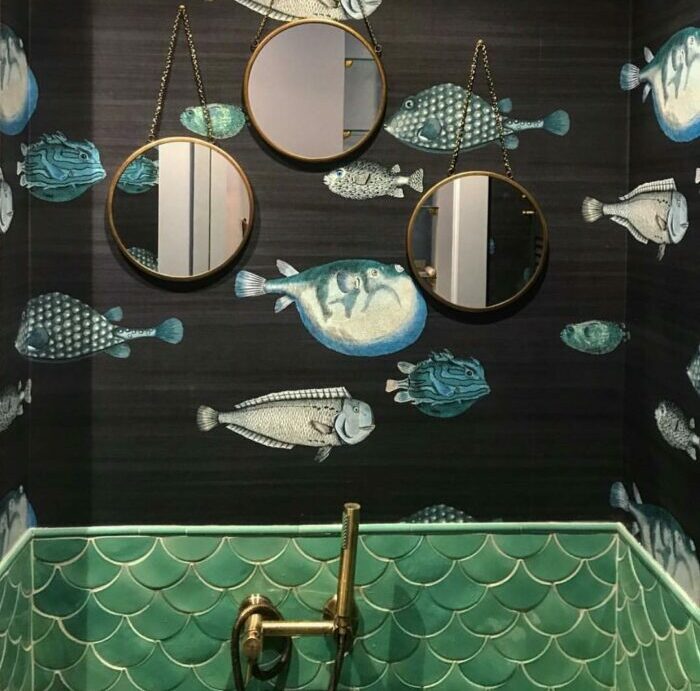 Bathroom with three mirrors, a water-themed sink, and wallpaper with fish designs