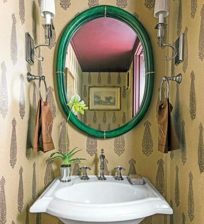 Bathroom with brown patterned wallpaper, white sink, green round mirror, floral decor, and matching brown towels. Bathroom with brown patterned wallpaper, white sink, green round mirror, floral decor, and matching brown towels.