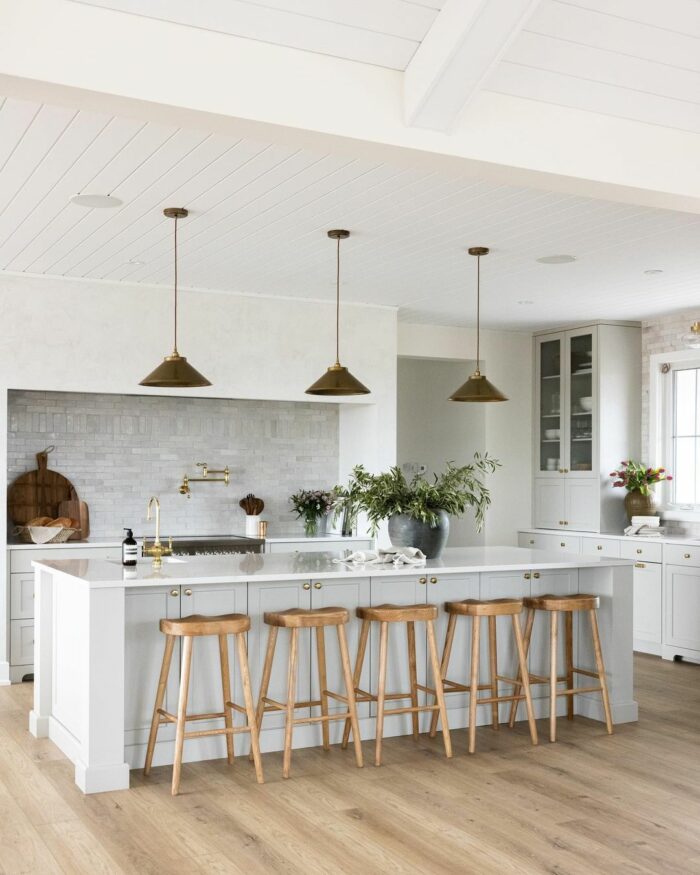 White kitchen with marble table wooden chairs and brass lights