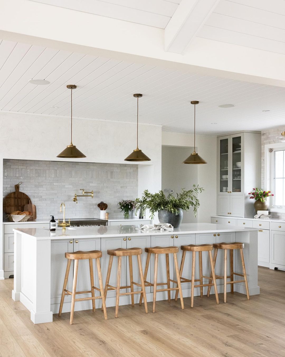 White kitchen with marble table wooden chairs and brass lights