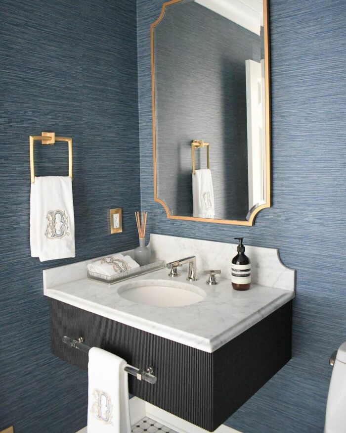 Bathroom with vinyl blue wallpaper, marble sink, gold fixtures, and matching embroidered towels in a modern space. Bathroom with vinyl blue wallpaper, marble sink, gold fixtures, and matching embroidered towels in a modern space.