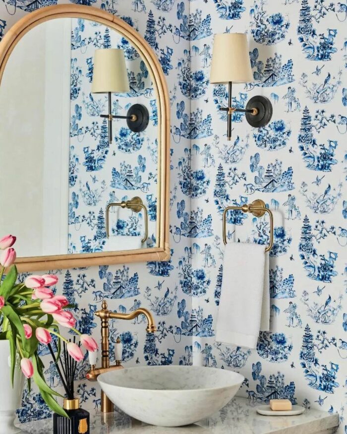 Bathroom with French-inspired blue wallpaper featuring traditional scenes, a marble sink, and brass fixtures. Bathroom with French-inspired blue wallpaper featuring traditional scenes, a marble sink, and brass fixtures.