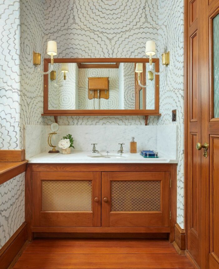 Bathroom with mid-century modern striped wallpaper and wooden vanity featuring a white marble countertop and sink. Bathroom with mid-century modern striped wallpaper and wooden vanity featuring a white marble countertop and sink.