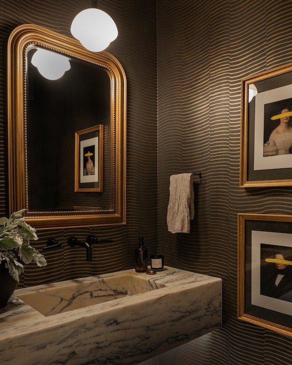 Bathroom with dark striped trendy wallpaper and a marble sink, featuring gold-framed mirror and framed artwork on walls. Bathroom with dark striped trendy wallpaper and a marble sink, featuring gold-framed mirror and framed artwork on walls.