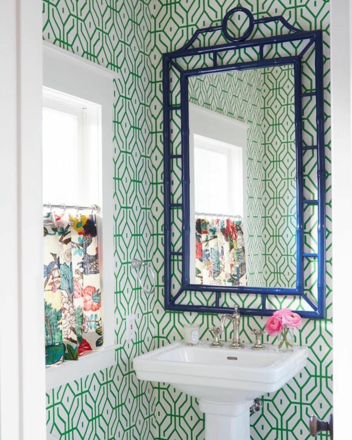 Bathroom with green tile patterned wallpaper, white pedestal sink, blue framed mirror, and floral curtains. Bathroom with green tile patterned wallpaper, white pedestal sink, blue framed mirror, and floral curtains.