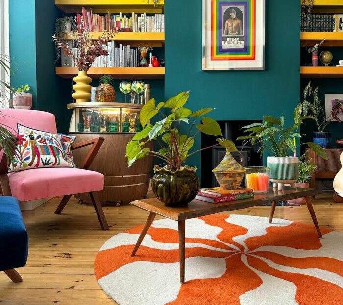 a maximalist living room with a patterned rug, bookshelf, table, and plants