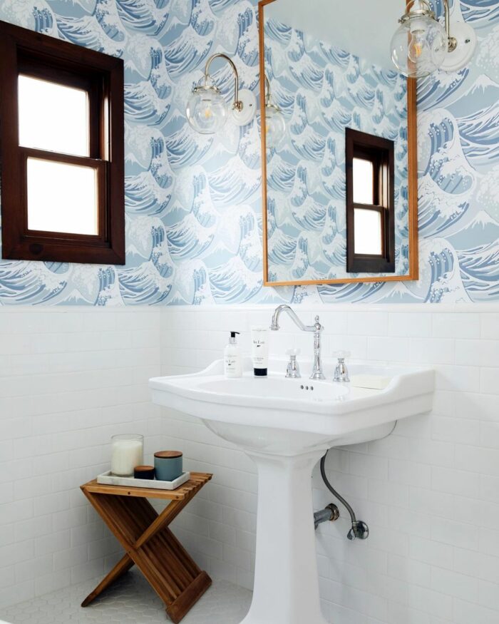Bathroom with blue ocean wallpaper, white pedestal sink, wooden window frame, and small wooden side table with candles. Bathroom with blue ocean wallpaper, white pedestal sink, wooden window frame, and small wooden side table with candles.
