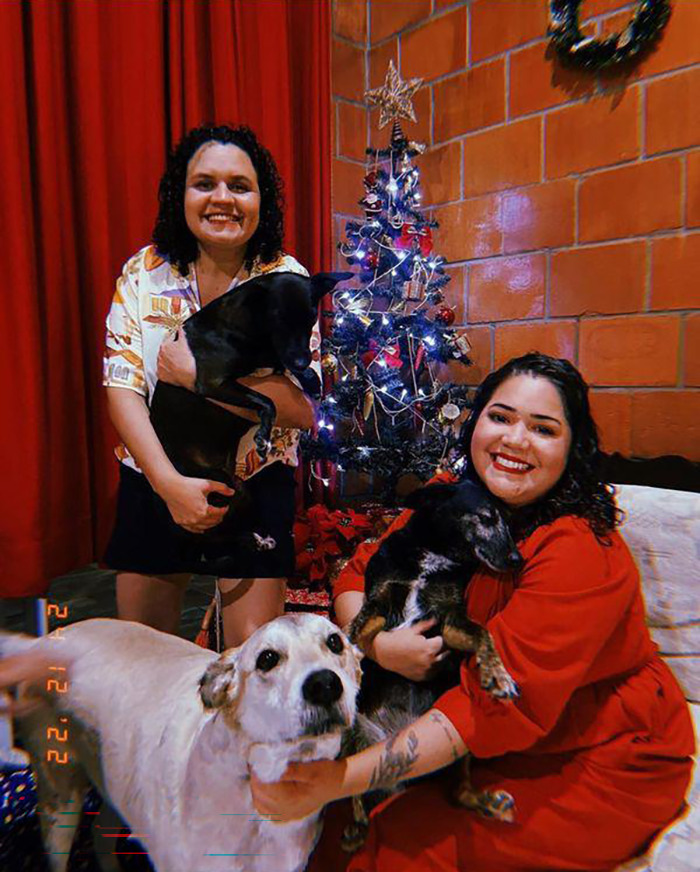 A family photo of Bruna, her wife and their 3 dogs by the Christmas tree
