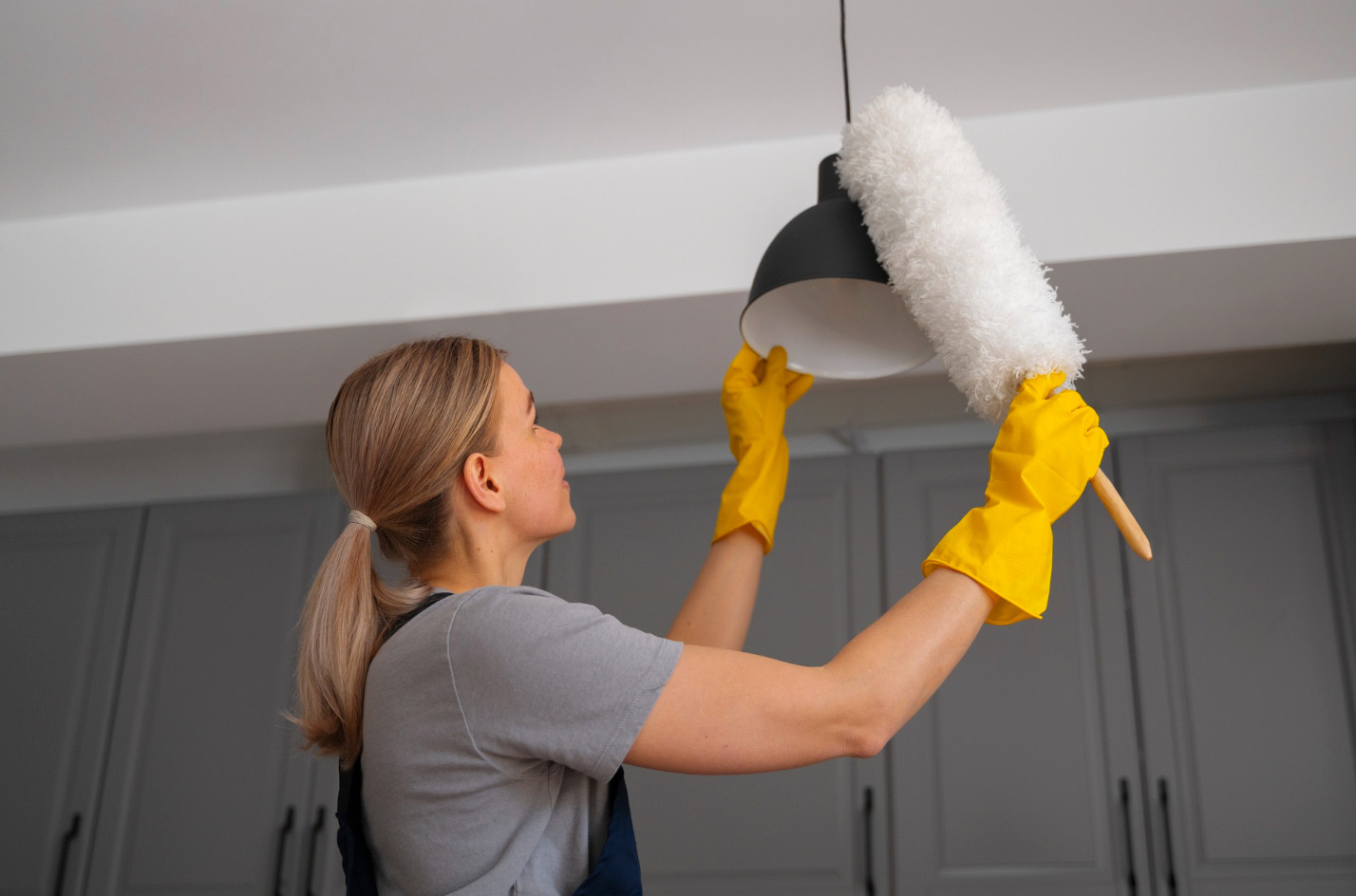 Woman in yellow gloves cleaning lampshade
