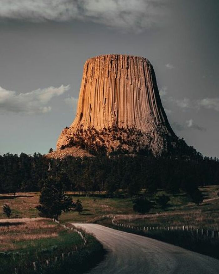 Devil's Tower In Wyoming, USA Is A Rare Natural Wonder With An Intriguing And Mysterious Backstory. The Tower's Commanding And Distinctive Appearance, Formation, And Personality Make It A Fascinating Sight To Behold. Nestled Amidst The Black Hills Near The Town Of Sundance, The Rock Mass Stands 1,267 Feet Tall Above The Belle Fourche River, Grasslands, And Ponderosa Pine Forests. It Was Designated As Our Country's First National Monument By Theodore Roosevelt In 1906. The Origin Of Devil's Tower Has Puzzled Native Americans And Early Explorers For Many Years. According To Native American Legend, Seven Little Girls Were Playing In The Forest When They Were Pursued By Giant Bears. The Girls Prayed And Jumped Onto A Boulder, Which Then Started To Grow And Lifted Them Toward The Sky. The Rock Eventually Grew Into The Tower, With The Cracks And Columns On It Attributed To The Bears' Failed Attempts To Climb It. Devil's Tower Is A Popular Destination For Traditional Rock Climbers, With Some Columns Featuring Crevices Up To 400 Feet In Length. Despite This, The Tower Holds Immense Cultural And Spiritual Significance To Many Native American Tribes, Who Still Consider It A Sacred Site. To Honor The Tribes' Cultural Practices And Rituals Still Performed There, Climbing The Monument Is Restricted During The Month Of June, Which Involves Sun Dances, Vision Quests, And Prayer Offerings That Are Significant Parts Of Devil's Tower's History. Geologists Have Established That Devil's Tower Was Created By A Volcano's Cooling Magma, Resulting In The Formation Of Distinct Columns. The Tower Is Unique In Size And Rock Type, Being Composed Of Phonolite. These Columns Are Among The Tallest And Widest Found In This Type Of Rock Formation
