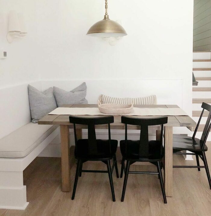 White banquette with gray pillows and wooden table with chairs