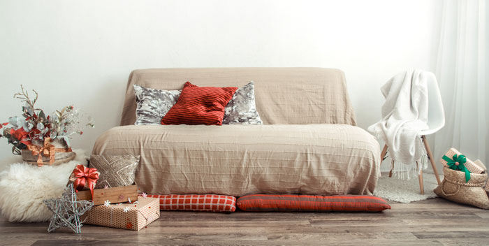 Beige couch with red and silver pillows on it and Christmas presents on the floor 