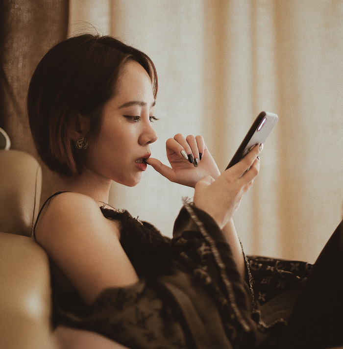 Young woman sitting on couch, nervously browsing scary facts on her phone, giving off heebie-jeebies vibe.