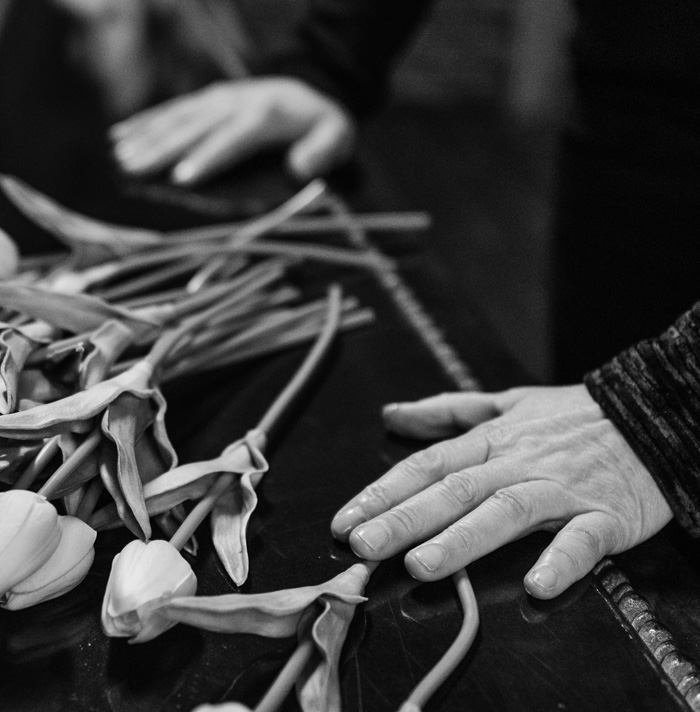 Black and white image of hands resting near wilted flowers, evoking eerie and scary facts atmosphere for heebie-jeebies.