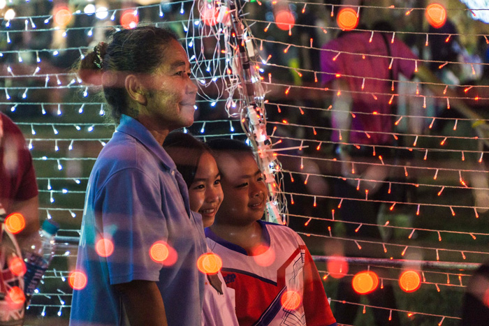 A woman with a girl and a boy standing in a tunnel of string lights and smiling in hra Nakhon Si Ayutthaya, Thailand 