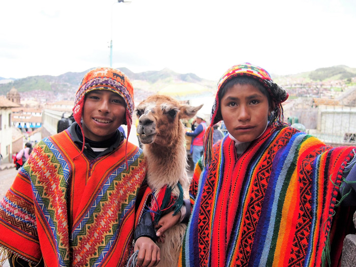 Two boys wearing traditional Peruvian clothes and 'Chullos' with llama in the middle in Cusco, Peru