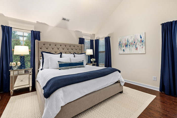 big bed with white and blue color linen and blue curtains on the windows