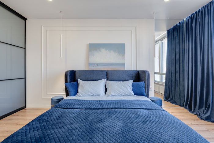 modern bedroom with bed with blue bedding and blue curtains on the window