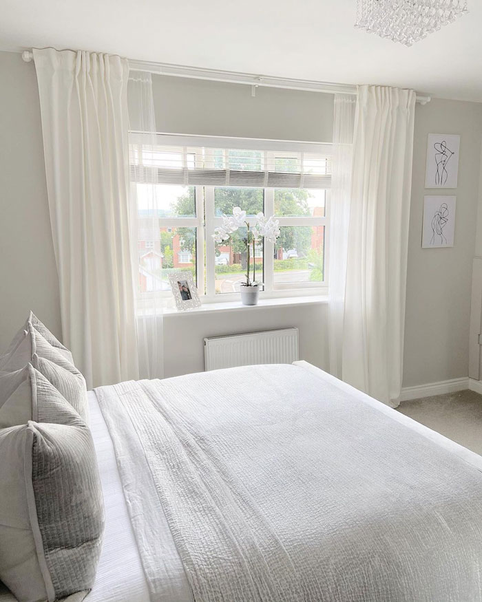 big bed near the window with white curtains in a white bedroom